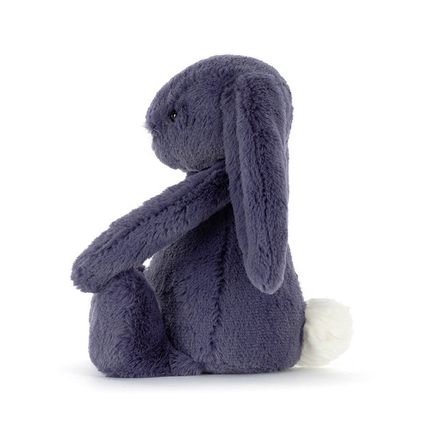 A plush, dark purple bunny with long ears and a white fluffy tail sits facing left.