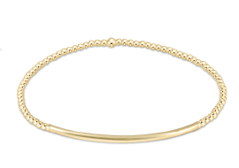A gold beaded bracelet with a smooth, curved bar at the front.