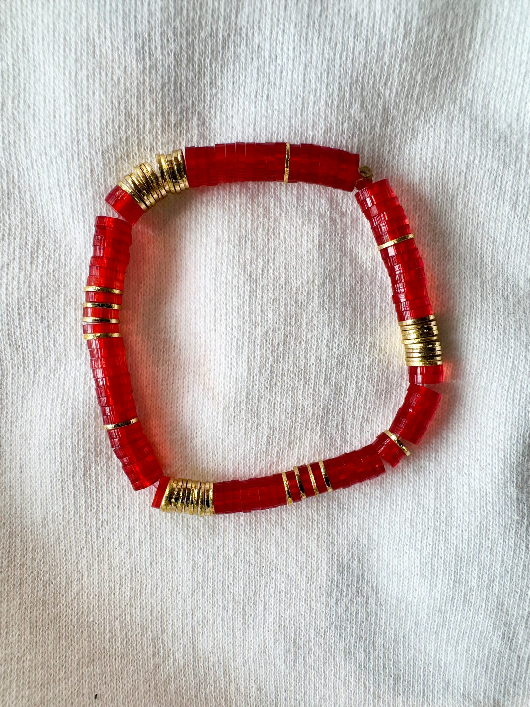 Large flat red bead bracelet with gold accents on a white fabric background.