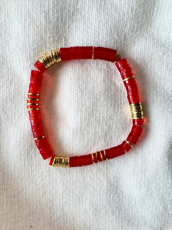 Large flat red bead bracelet with gold accents on a white fabric background.
