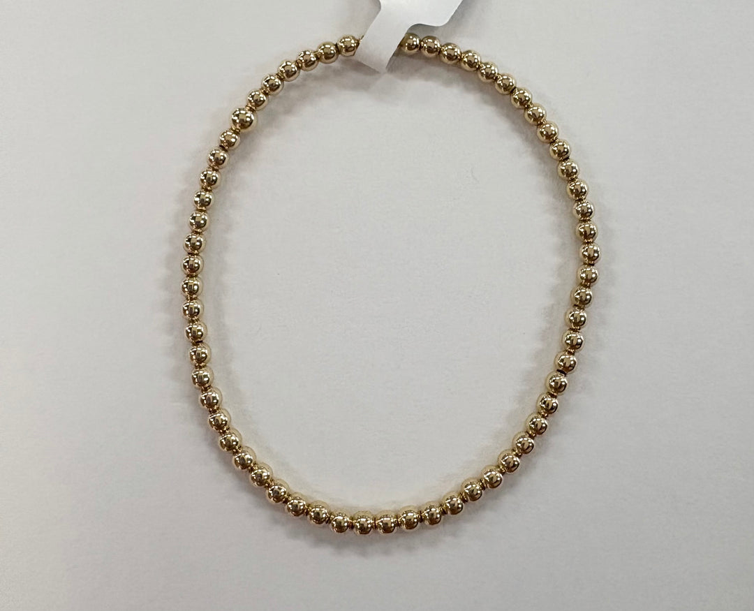 A gold beaded bracelet forms a circle on a white surface.