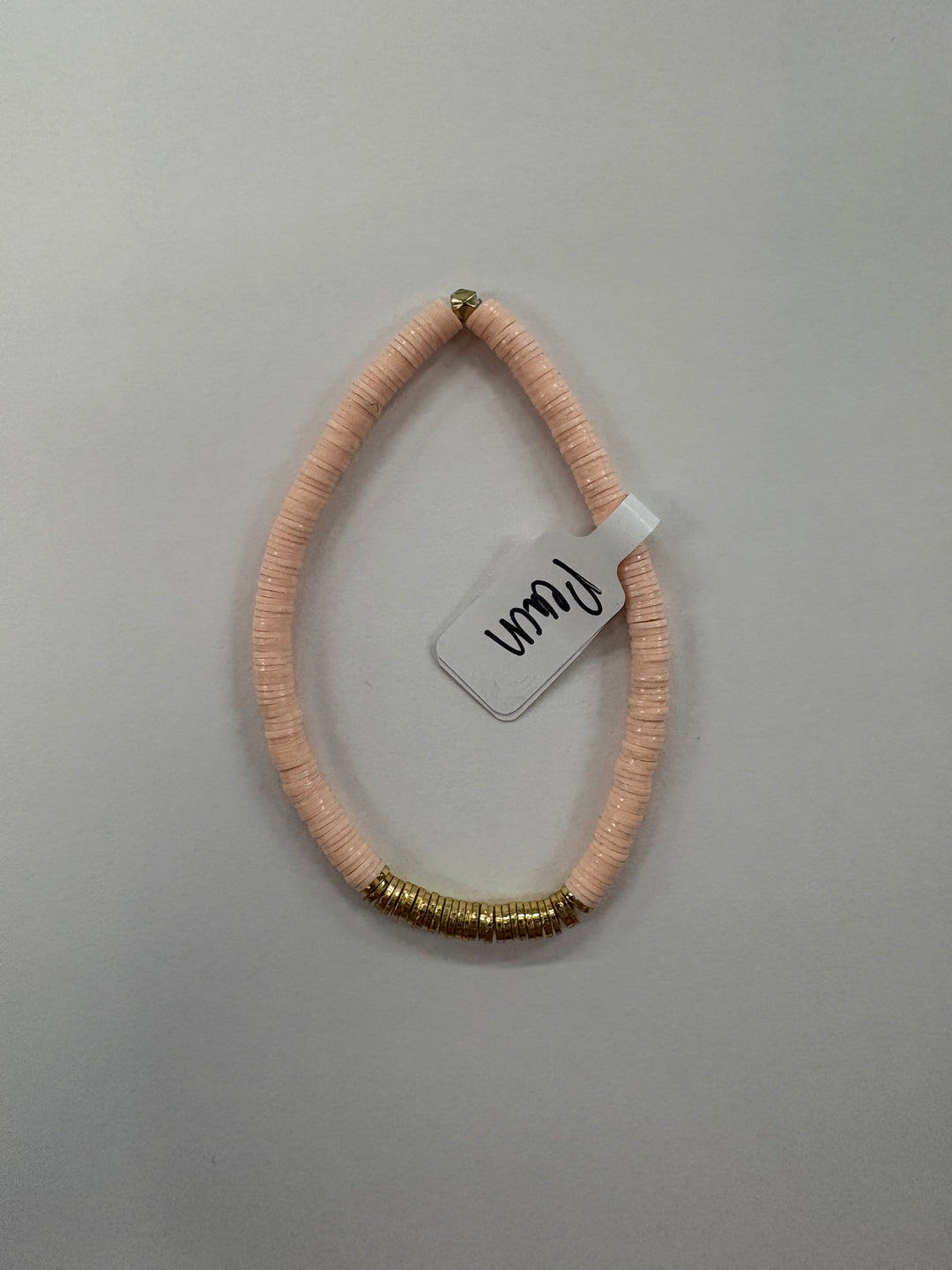 A light pink flat bead bracelet with a section of gold-colored beads and a white tag.