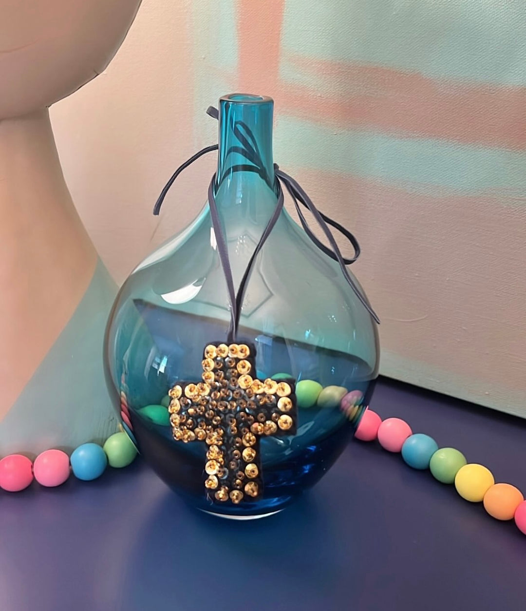 Mini Cross Hand Beaded Ornament hanging on a blue glass vase with colorful beads.