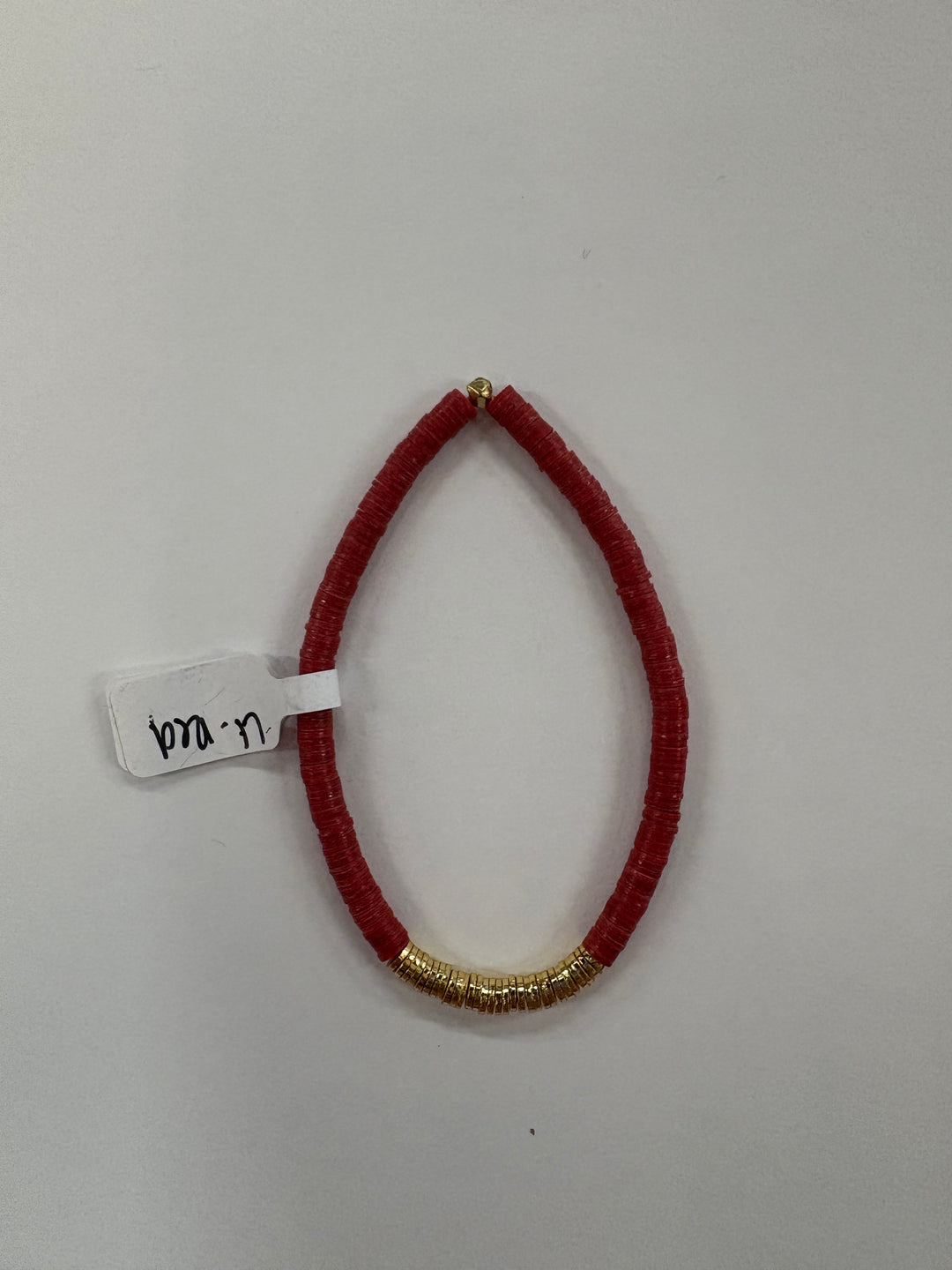 Small red flat bead bracelet with a section of gold-plated beads and a white tag.
