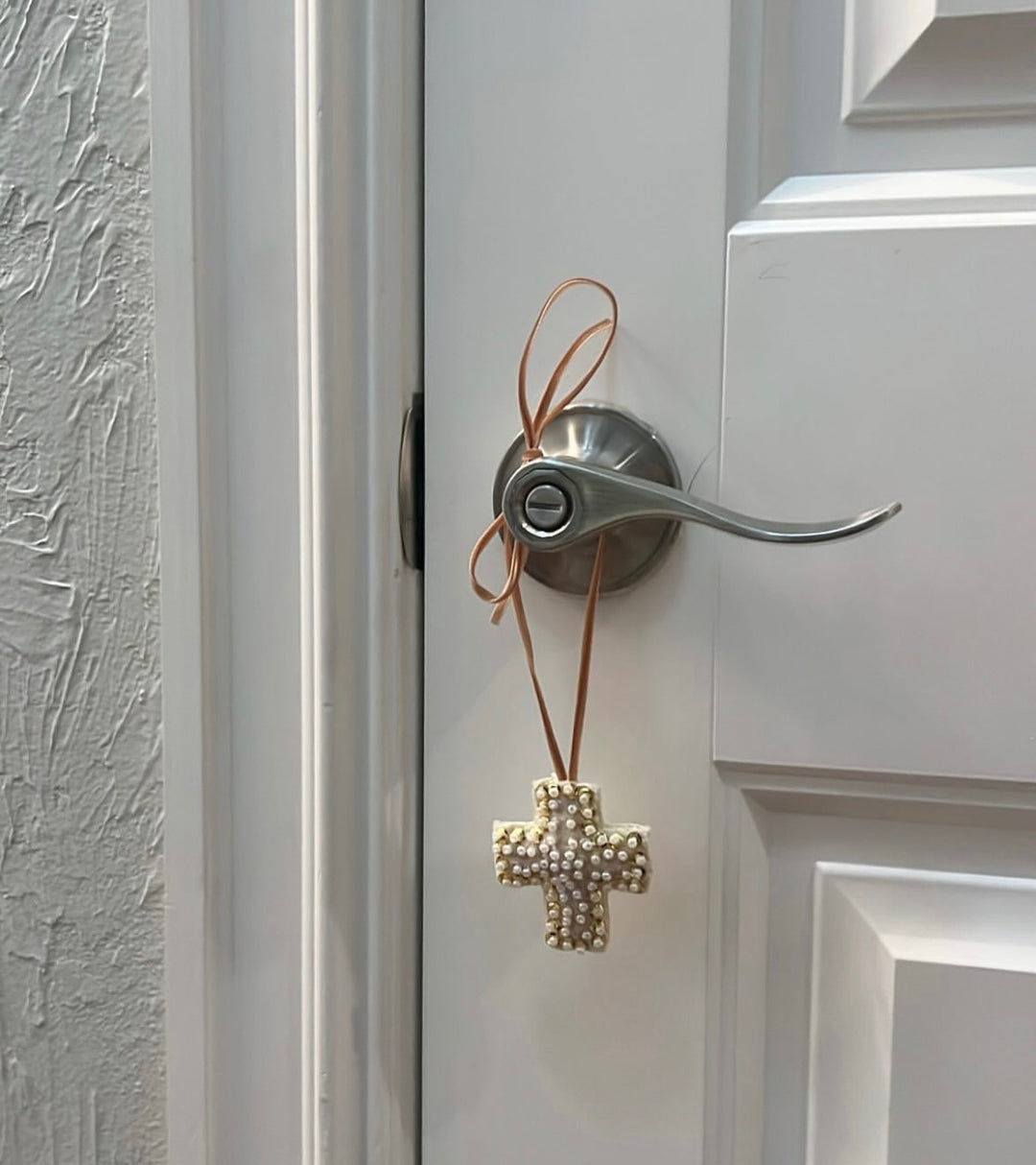 Mini Cross Hand Beaded Ornament hanging from a silver door handle.