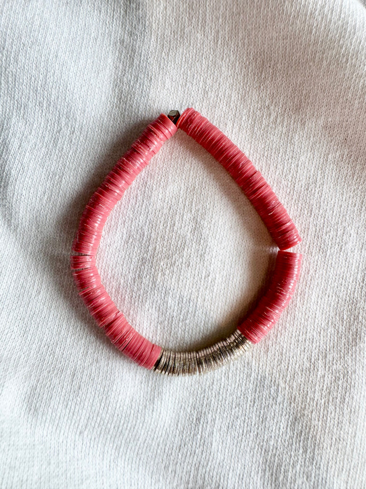 A pink and silver flat bead bracelet is arranged in a teardrop shape on a white knit surface.