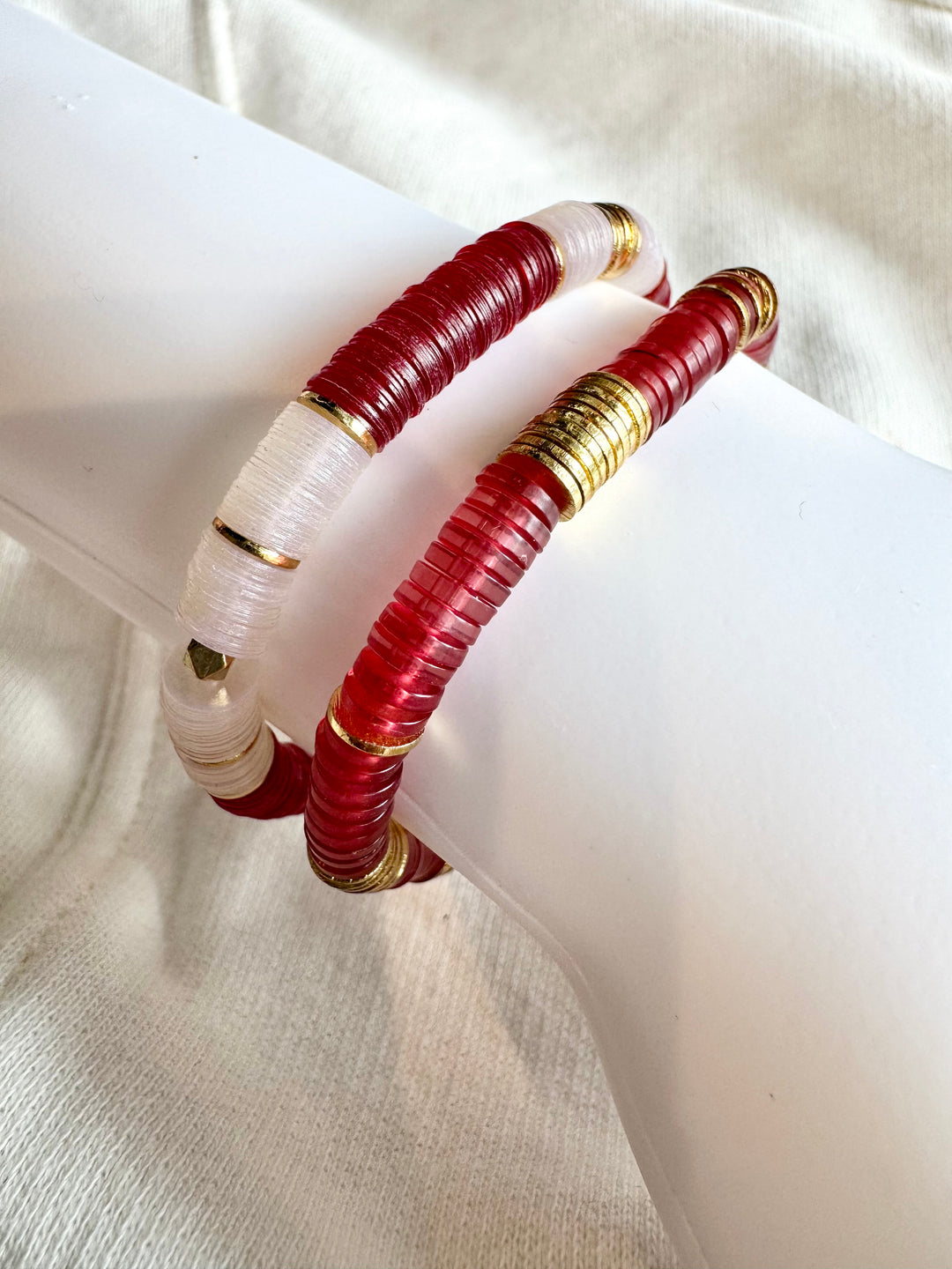 Two large flat bead bracelets, one red and one white, with gold accents.