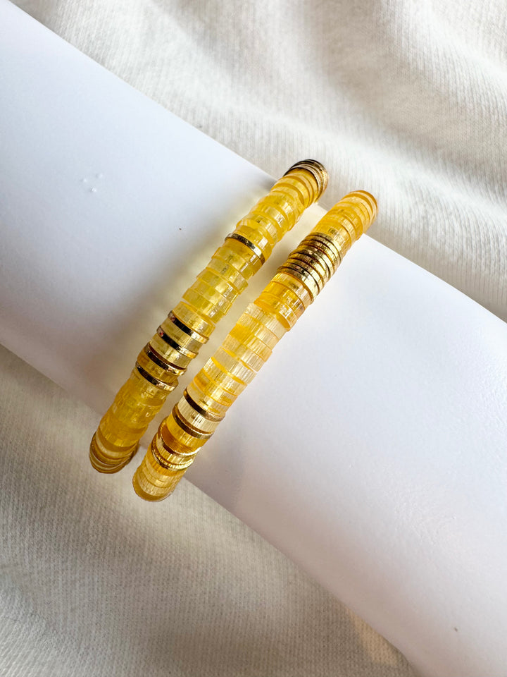 Two large flat bead bracelets with gold accents are displayed on a white surface.
