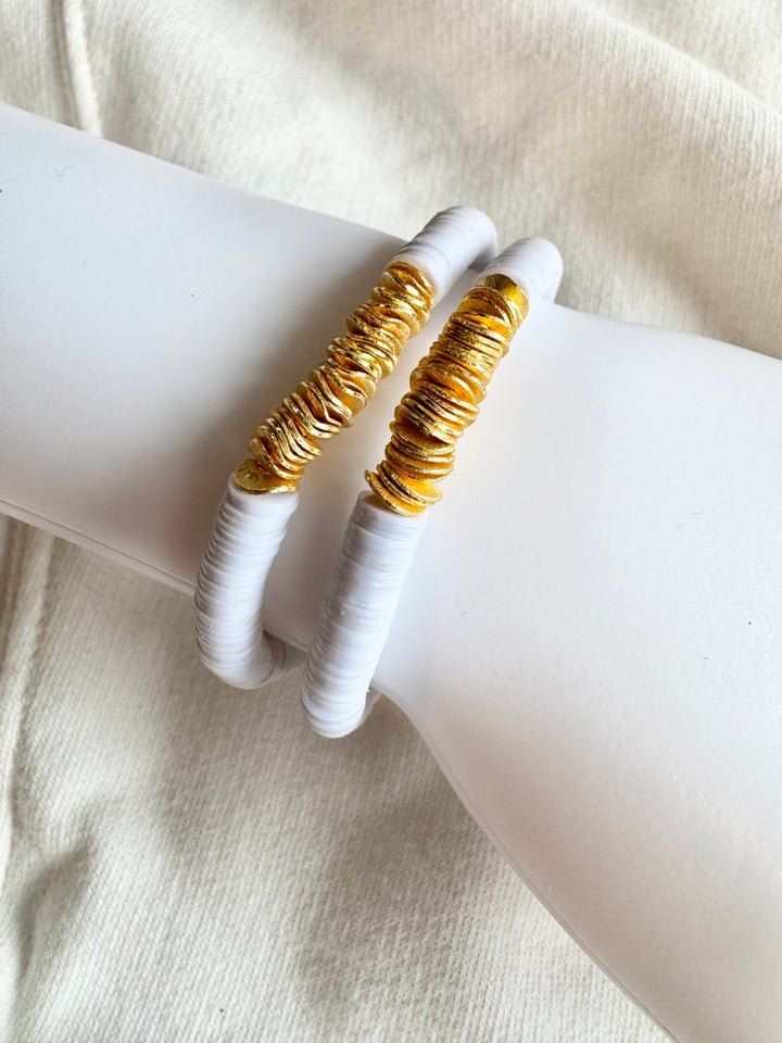 Two white flat bead bracelets with gold-plated accents are displayed on a white surface.