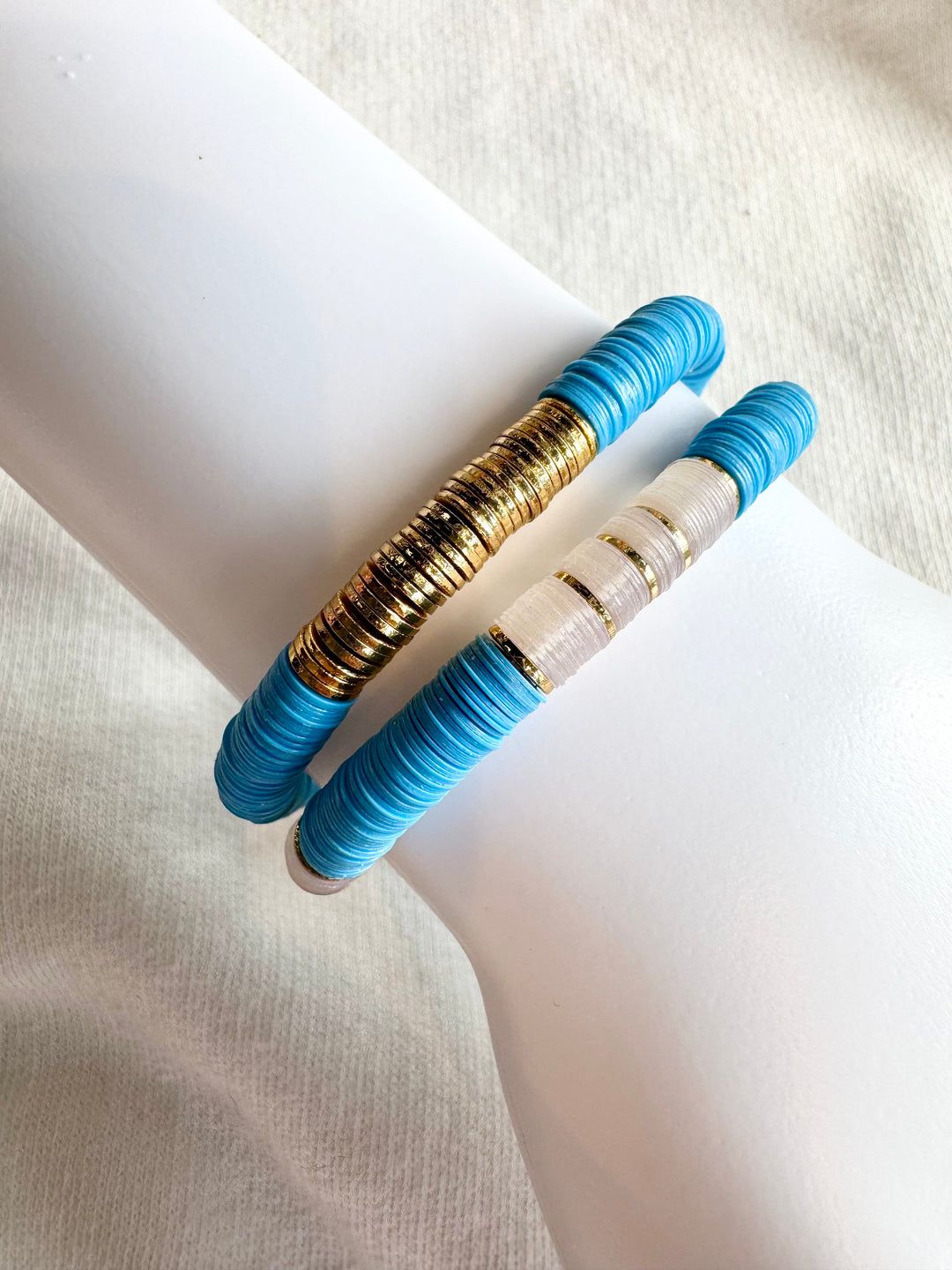 Two flat bead bracelets, one with gold and blue beads, the other with white and blue beads.
