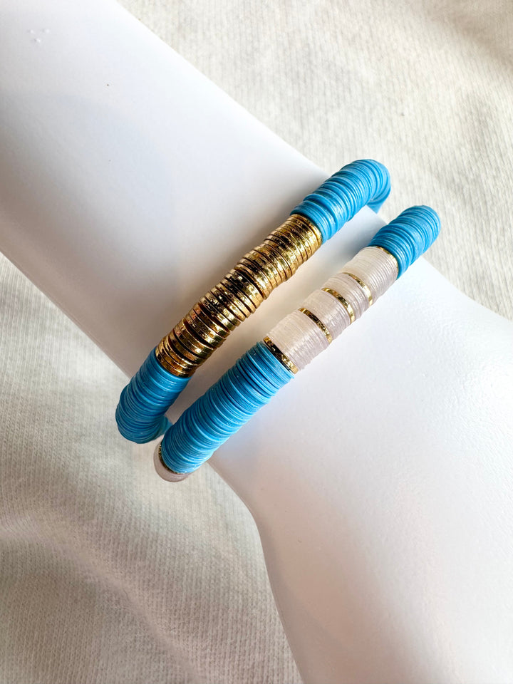 Two flat bead bracelets, one with gold and blue beads, the other with white and blue beads.
