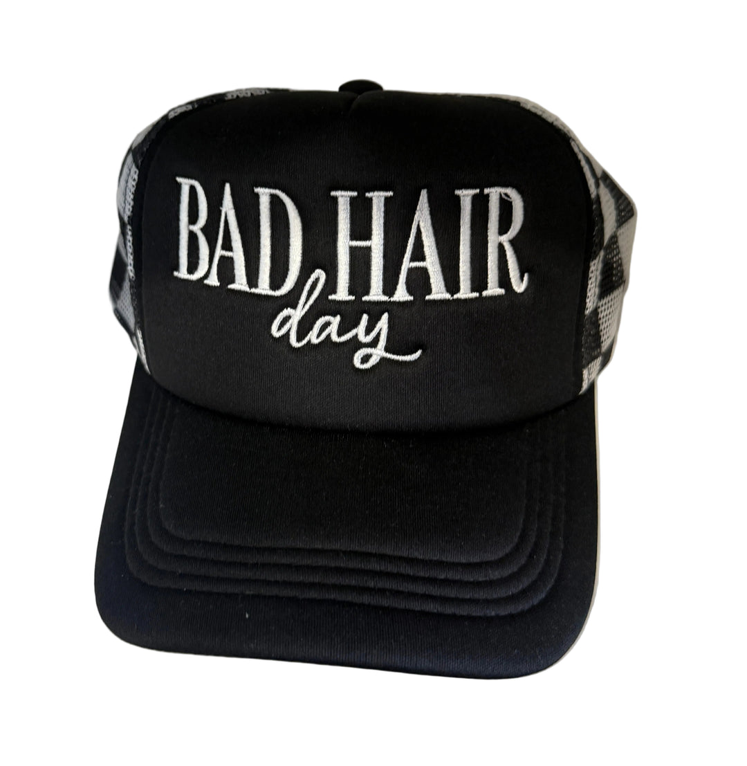 Black trucker hat with white "Bad Hair Day" embroidery and checkered mesh sides.