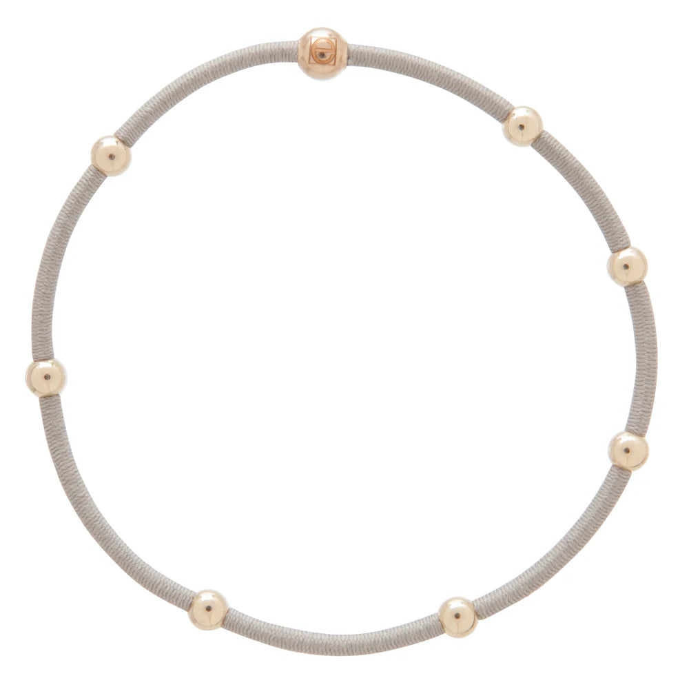 A neutral hair tie bracelet with eight gold beads.