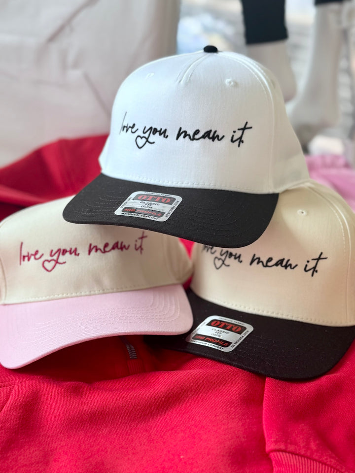 Three embroidered hats with the phrase "love you mean it" in different colors.