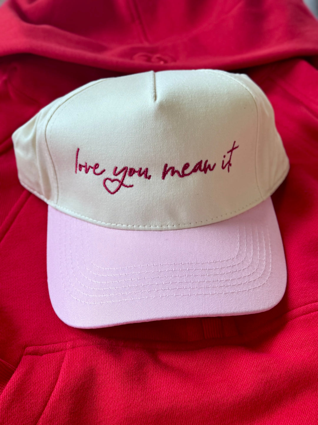 A cream and pink baseball cap with "love you mean it" embroidered in maroon.