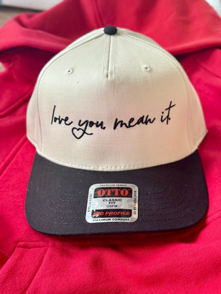 A beige and black baseball cap with "love you mean it" embroidered on the front.