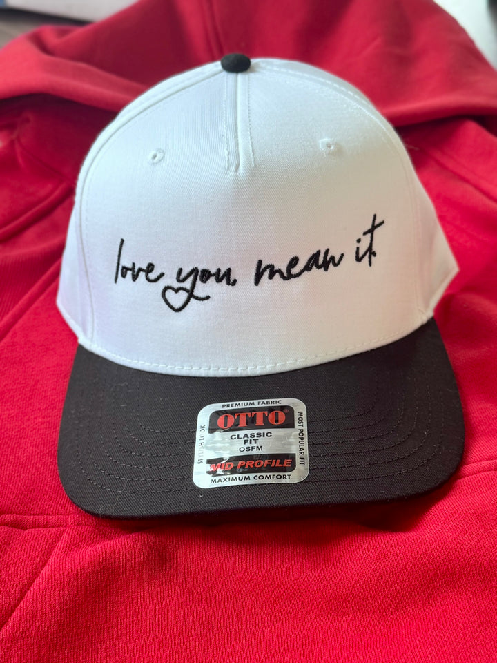 A white and black baseball cap with "love you mean it" embroidered on the front.
