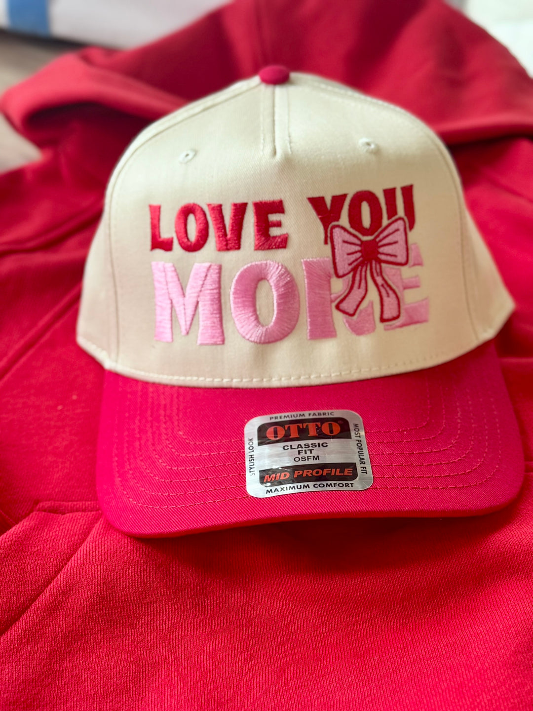 A cream and pink embroidered hat with "Love You More" text.