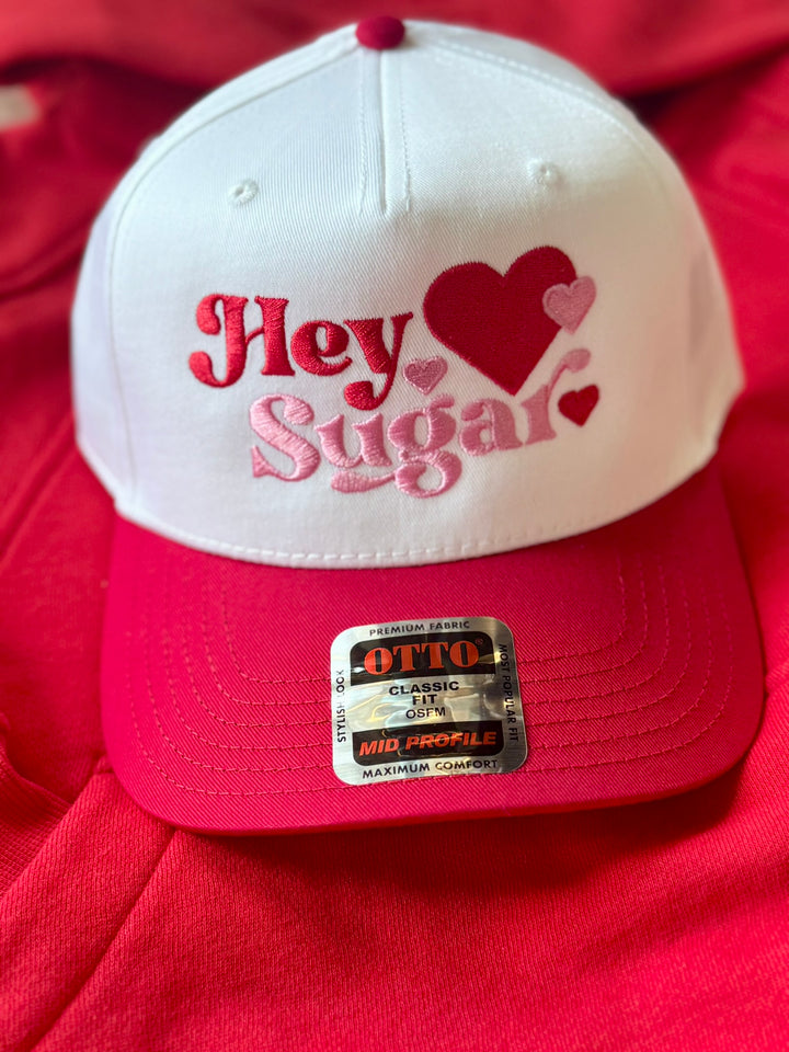 White and pink embroidered hat with "Hey Sugar" text and hearts.