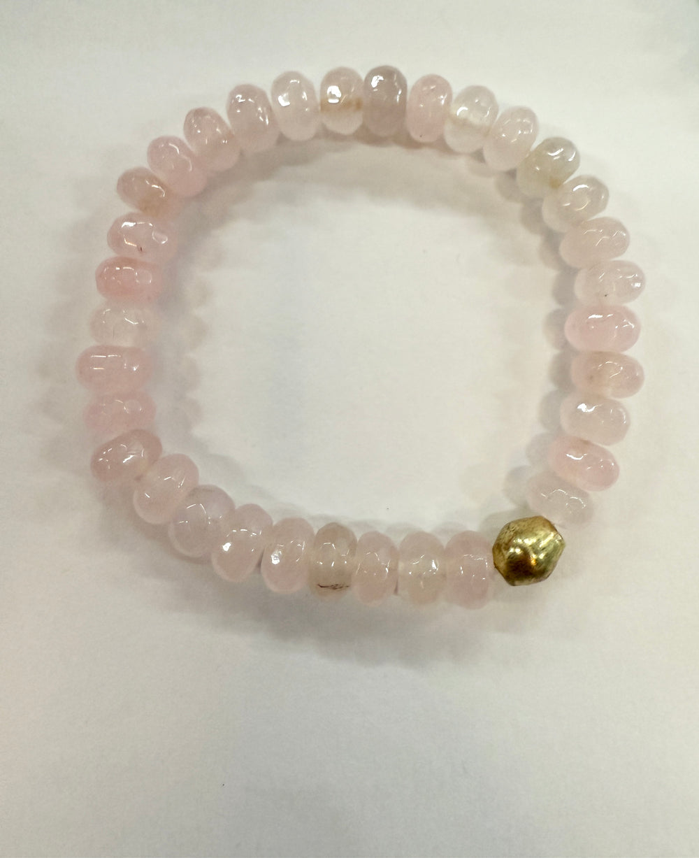 A bracelet made of light pink, polished jade beads with one gold bead.
