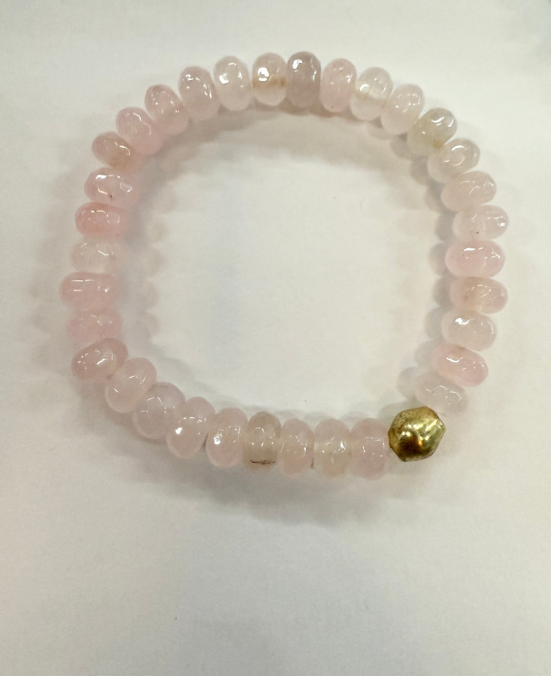 A bracelet made of light pink, polished jade beads with one gold bead.