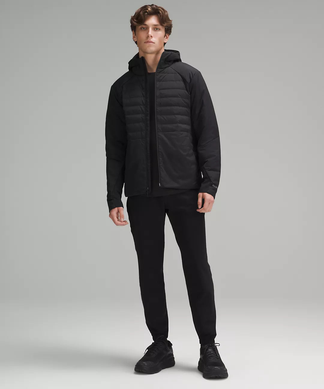 A man models a black Down for It All Hoodie with quilted front and smooth sleeves.