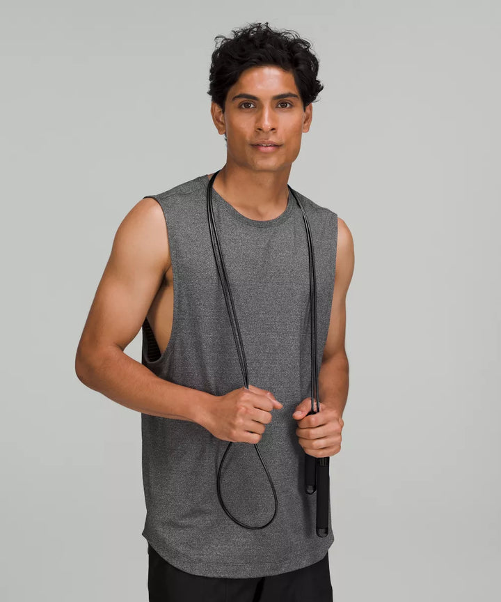 A man in a grey tank top holds a black jump rope.