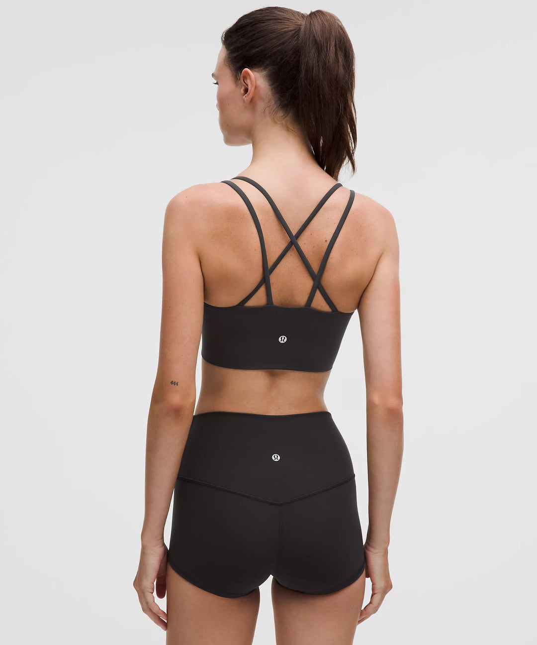 Black longline sports bra with crisscross straps and white logo.