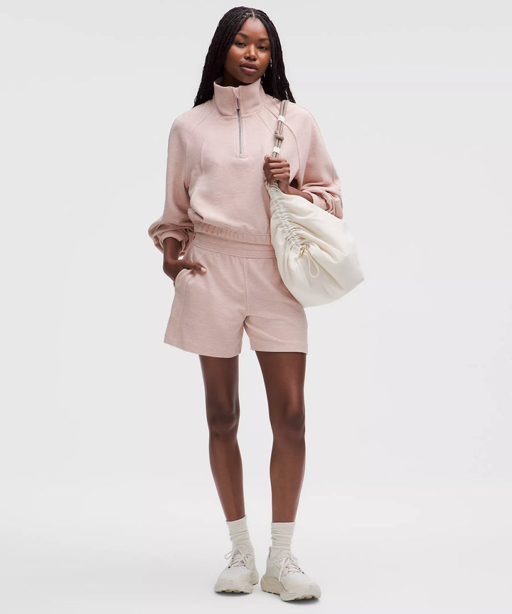 A woman models a pink waffle-knit half-zip sweatshirt and matching shorts.