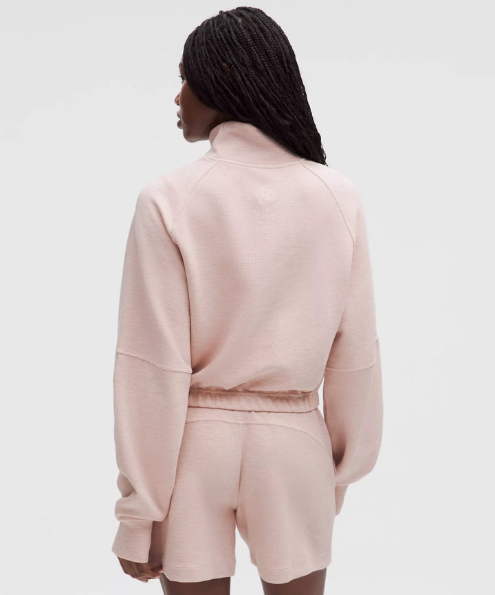 A woman wears a pink waffle-knit cropped half-zip sweatshirt and matching shorts.