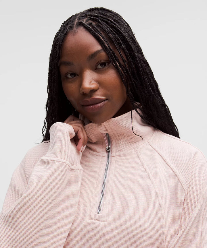 A woman wears a light pink waffle-knit half-zip sweatshirt.