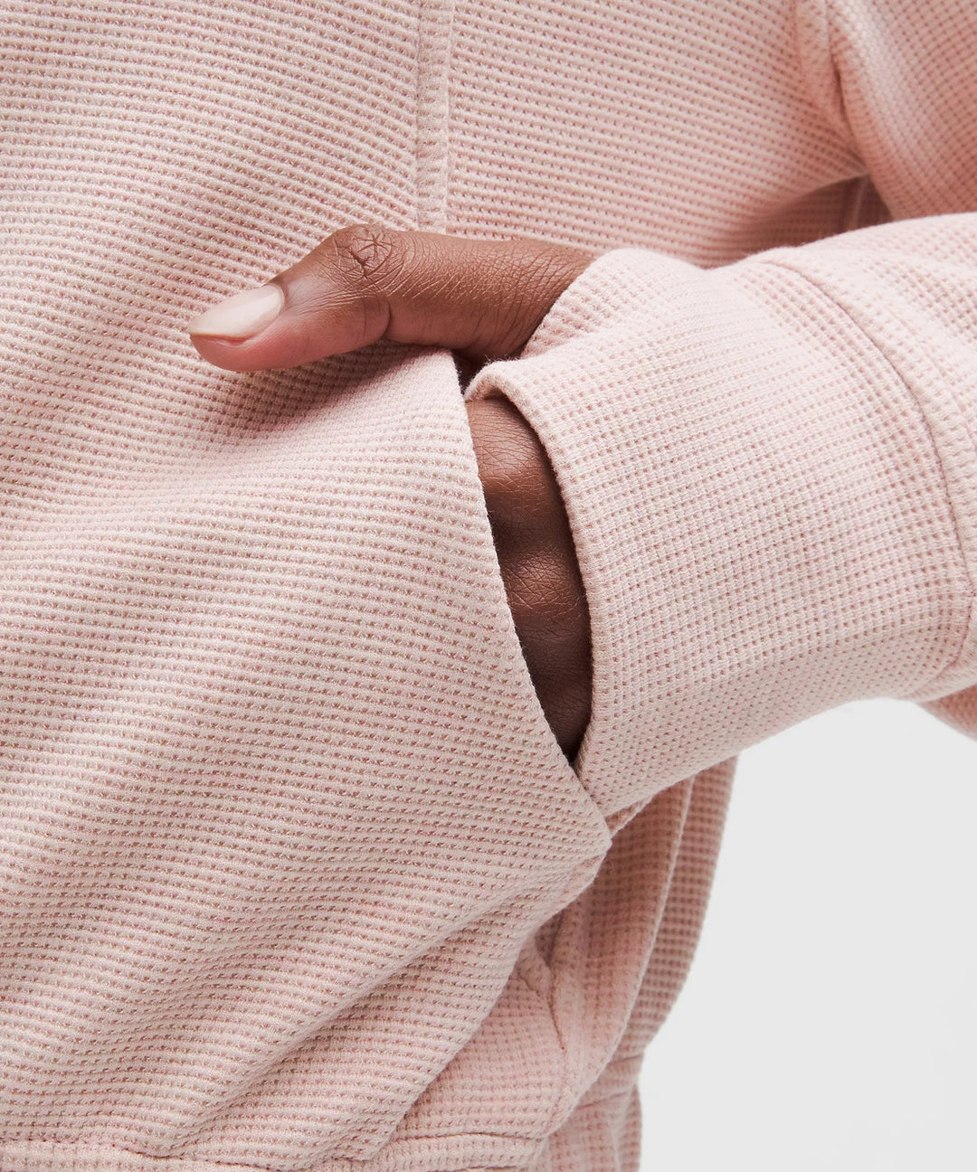 A hand rests in the pocket of a pink waffle-knit funnel-neck half-zip top.