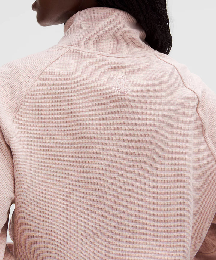 A pink waffle-knit cropped funnel-neck half-zip sweatshirt with a subtle logo on the back.