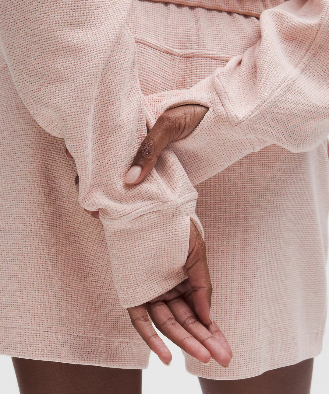 A close-up of a person wearing a pink waffle-knit top with thumbholes.