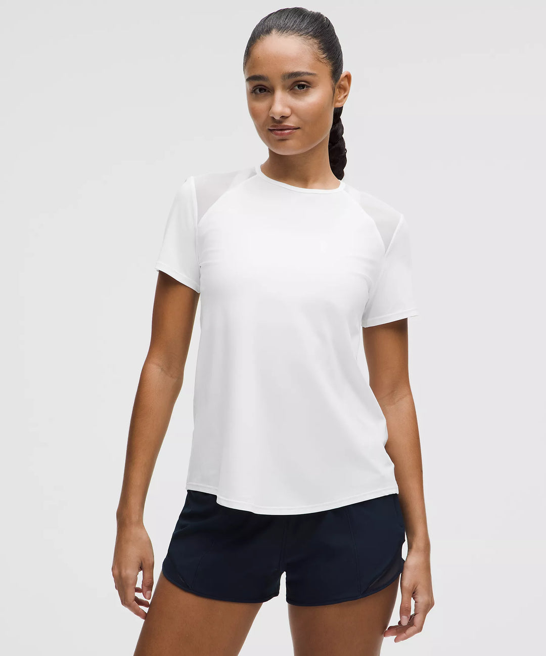 A woman models a white short-sleeve shirt with mesh shoulder panels and navy shorts.