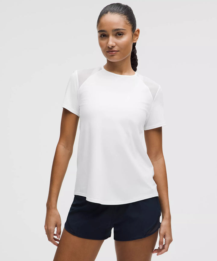 A woman models a white short-sleeve shirt with mesh shoulder panels and navy shorts.