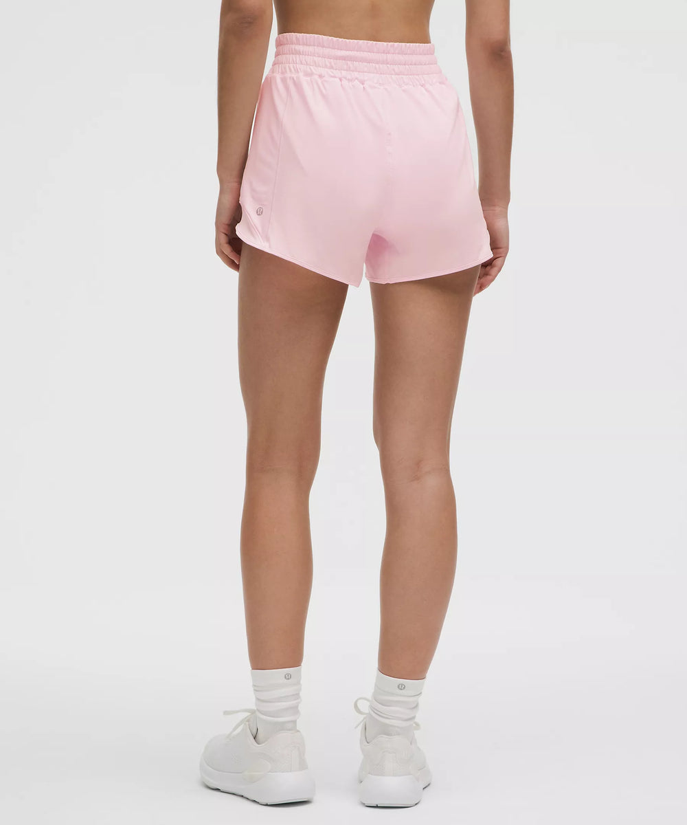 A person from behind wearing pink high-rise lined shorts, white socks, and white sneakers.