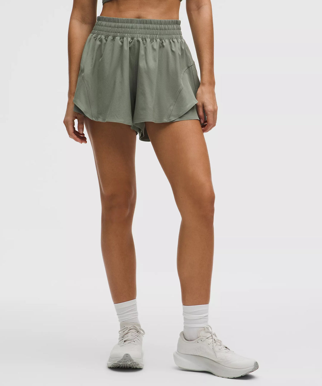 Fog green high-rise running shorts with a layered hem and white socks.