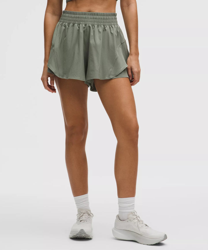 Fog green high-rise running shorts with a layered hem and white socks.