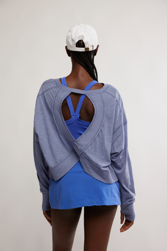 A woman from behind wears a blue long-sleeve top with an open back over a blue sports bra.