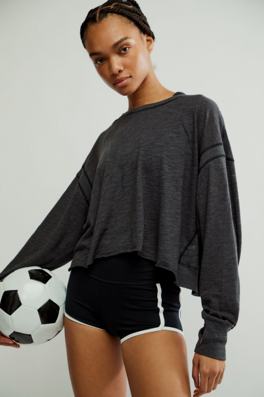 A woman in a black cropped long-sleeve top and black shorts holds a soccer ball.