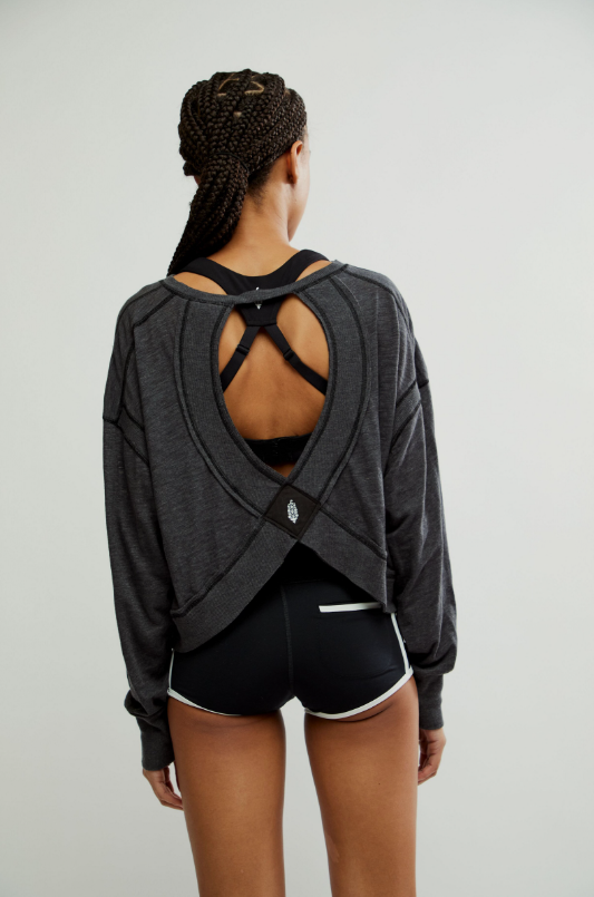 A woman from behind wears a black long-sleeved top with an open back and black shorts.
