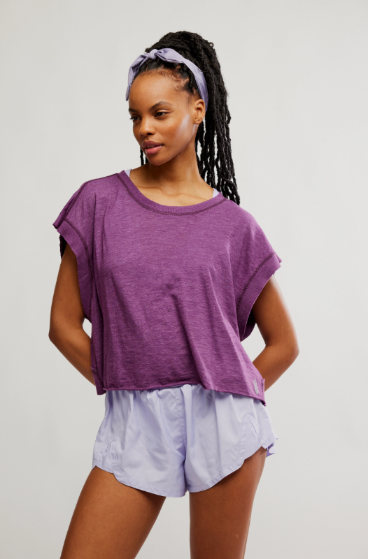 A woman wears a purple short-sleeved tee with light purple shorts and a matching headband.