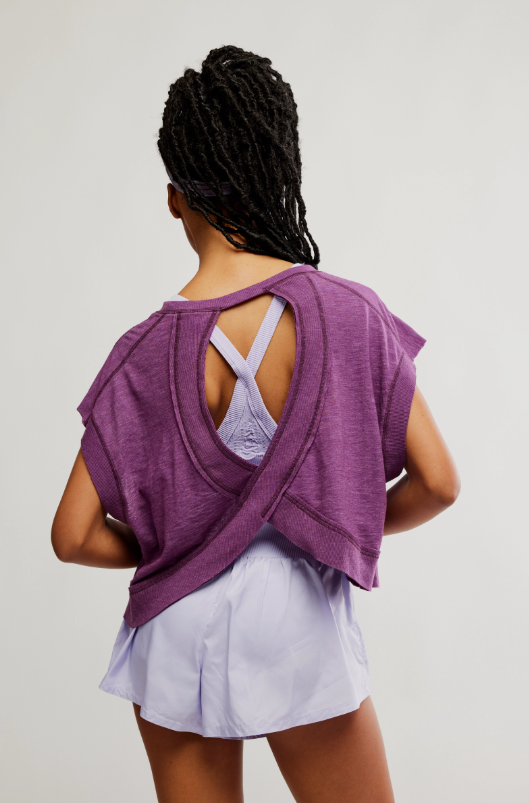 A woman from behind wears a purple tee with a wrapped cutout back over a light purple bra.