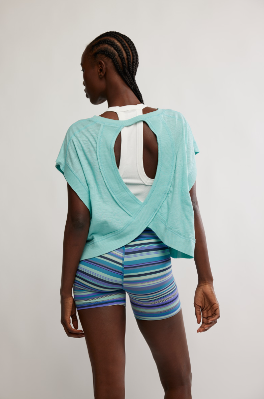A woman from behind wears a blue wave tee with a wrapped cutout back and striped shorts.