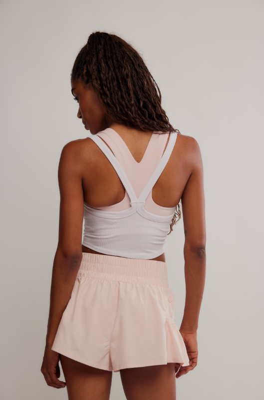 A woman from behind wears a white cami and light pink shorts.