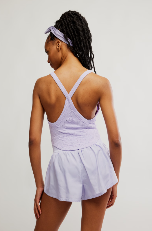 A woman from behind wears a purple cami with a racerback and matching shorts.