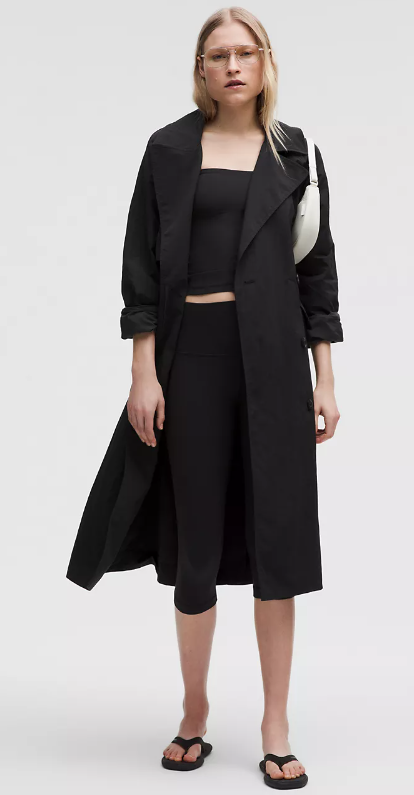 Woman wearing a black trench coat, black crop top, black capri leggings, and black flip-flops.