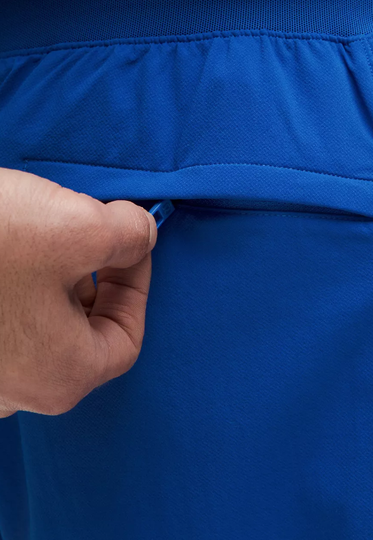 Close-up of a hand zipping a pocket on blue athletic shorts.