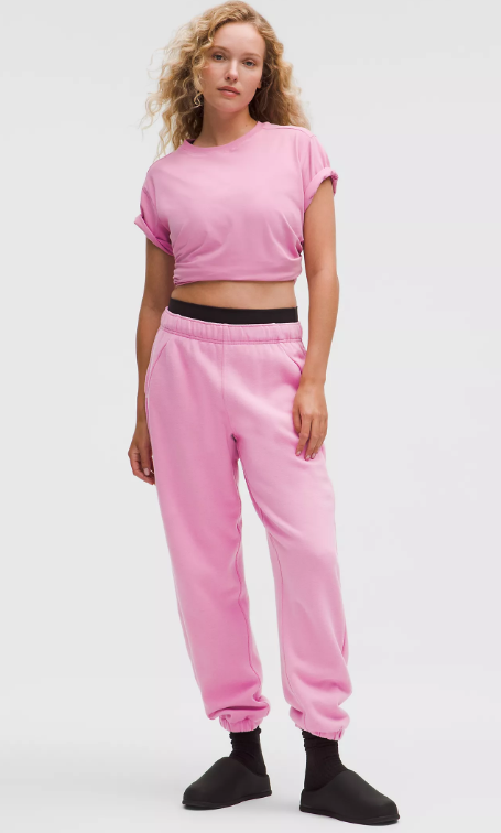 Pink oversized fleece joggers with a black waistband and black slippers.